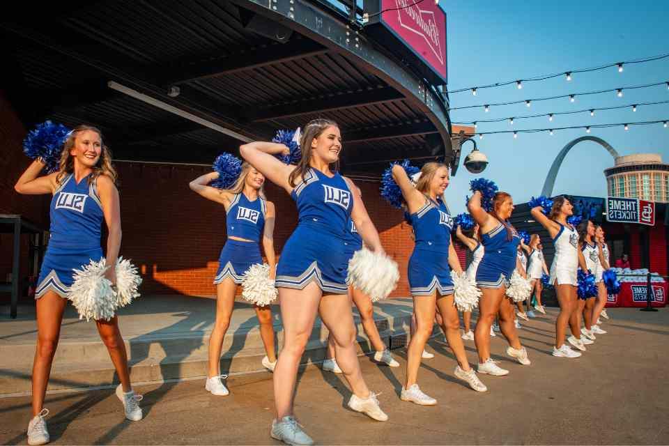 博彩网址大全's cheer team in uniform with poms in front of Busch Stadium with the Gateway Arch in the background.