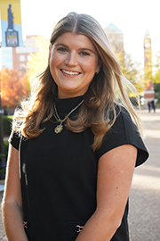 A headshot photo of Charlotte Schoen with a clocktower and trees in the background.