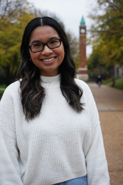 A headshot photo of Emily Tran with a clocktower and trees in the background.